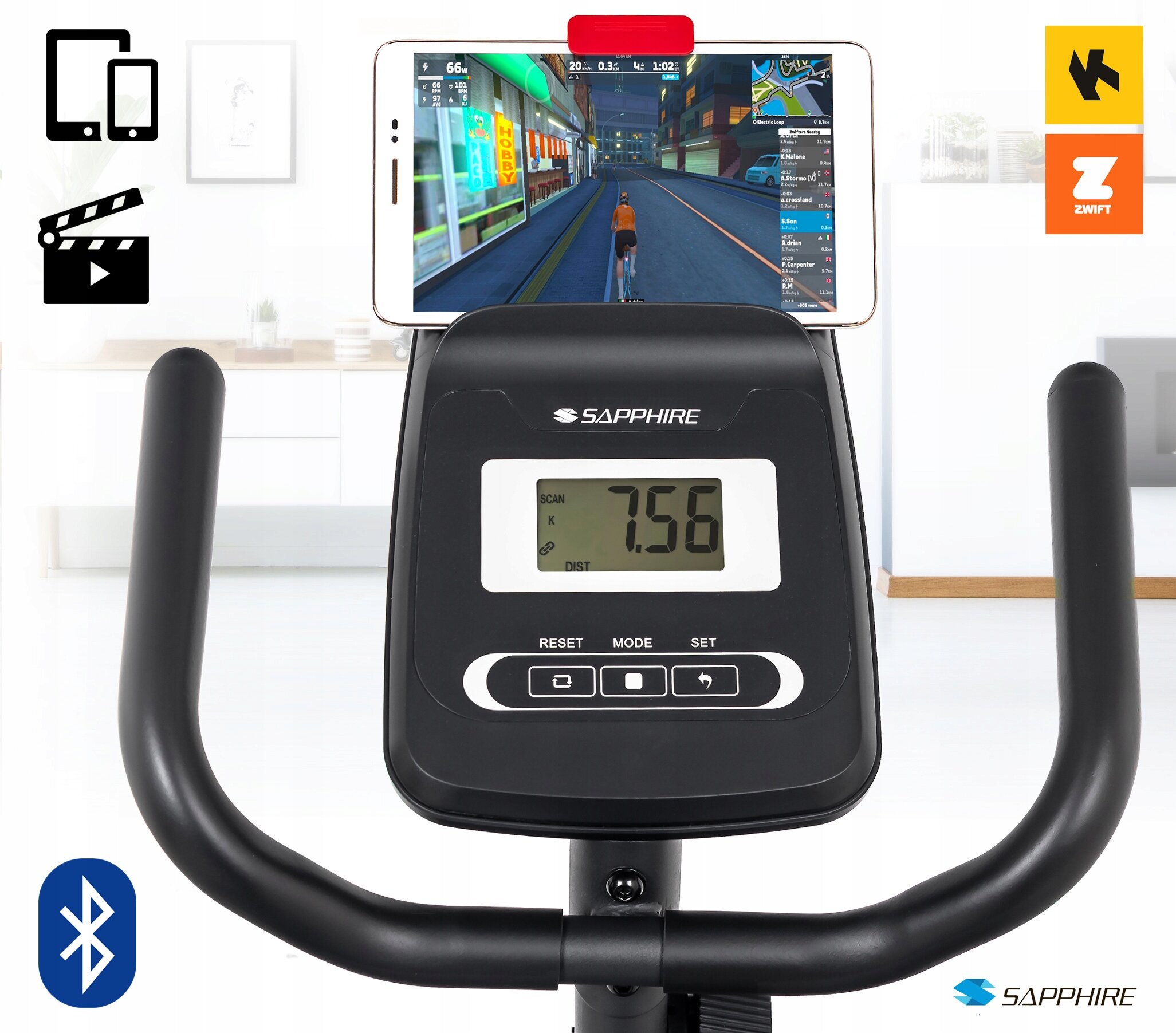 Na zdjęciu widoczny jest panel sterowania roweru treningowego z wyświetlaczem pokazującym wartość 7.56 oraz logo SAPPHIRE. Na uchwycie znajduje się urządzenie mobilne z aplikacją do jazdy wirtualnej, a obok widoczne są ikony Bluetooth i aplikacji ZWIFT.