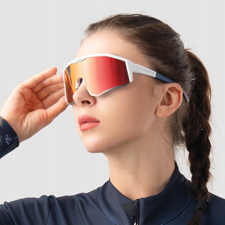 Osoba nosi sportowe okulary z dużymi, polaryzacyjnymi soczewkami w kolorze czerwonym. Na zauszniku widoczne jest logo \'ROCKBROS\'.
