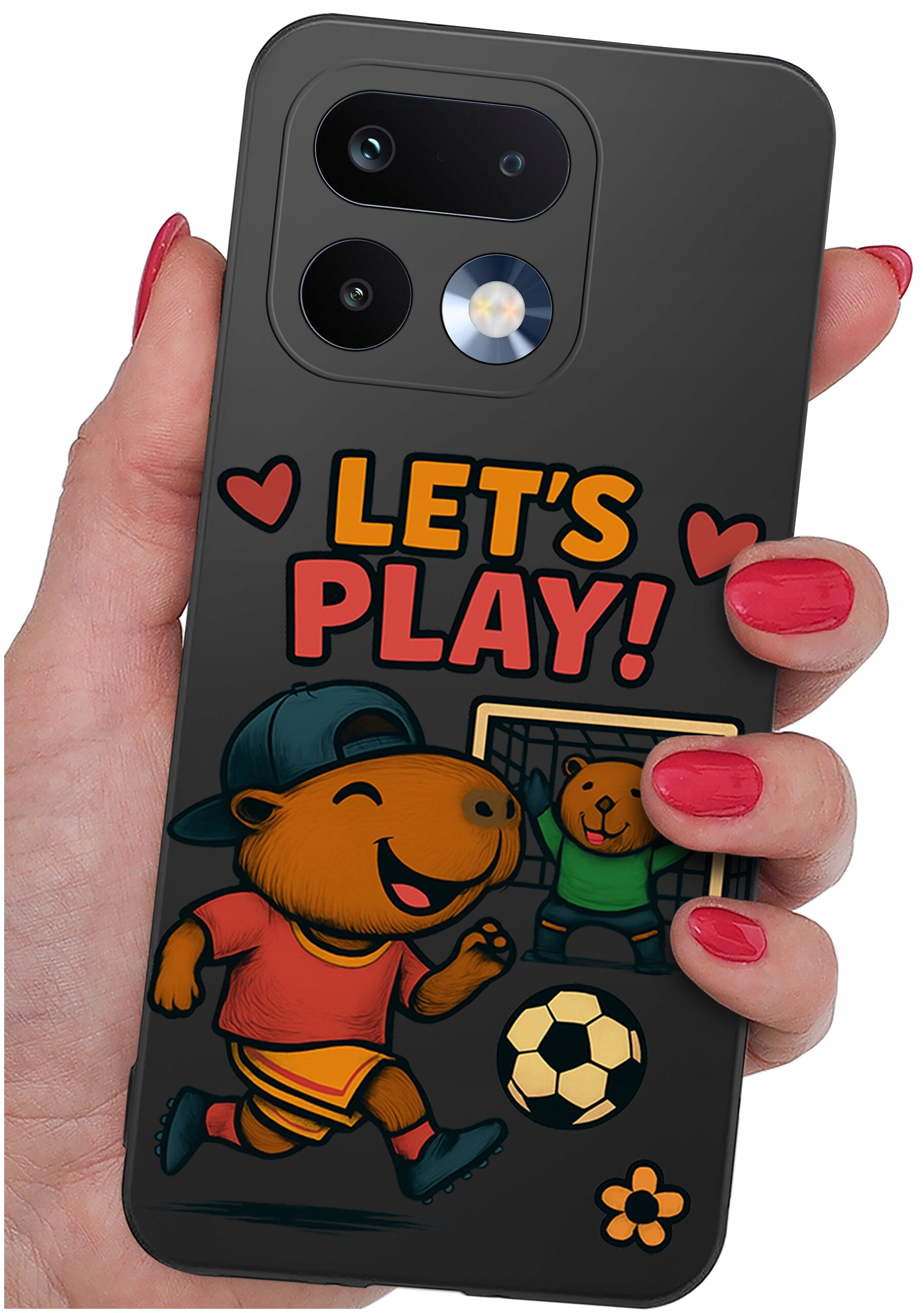 Etui na telefon z kolorowym nadrukiem przedstawiającym zwierzęta grające w piłkę nożną oraz napis \'LET\'S PLAY!\'. Etui trzymane jest w dłoni z pomalowanymi na czerwono paznokciami.
