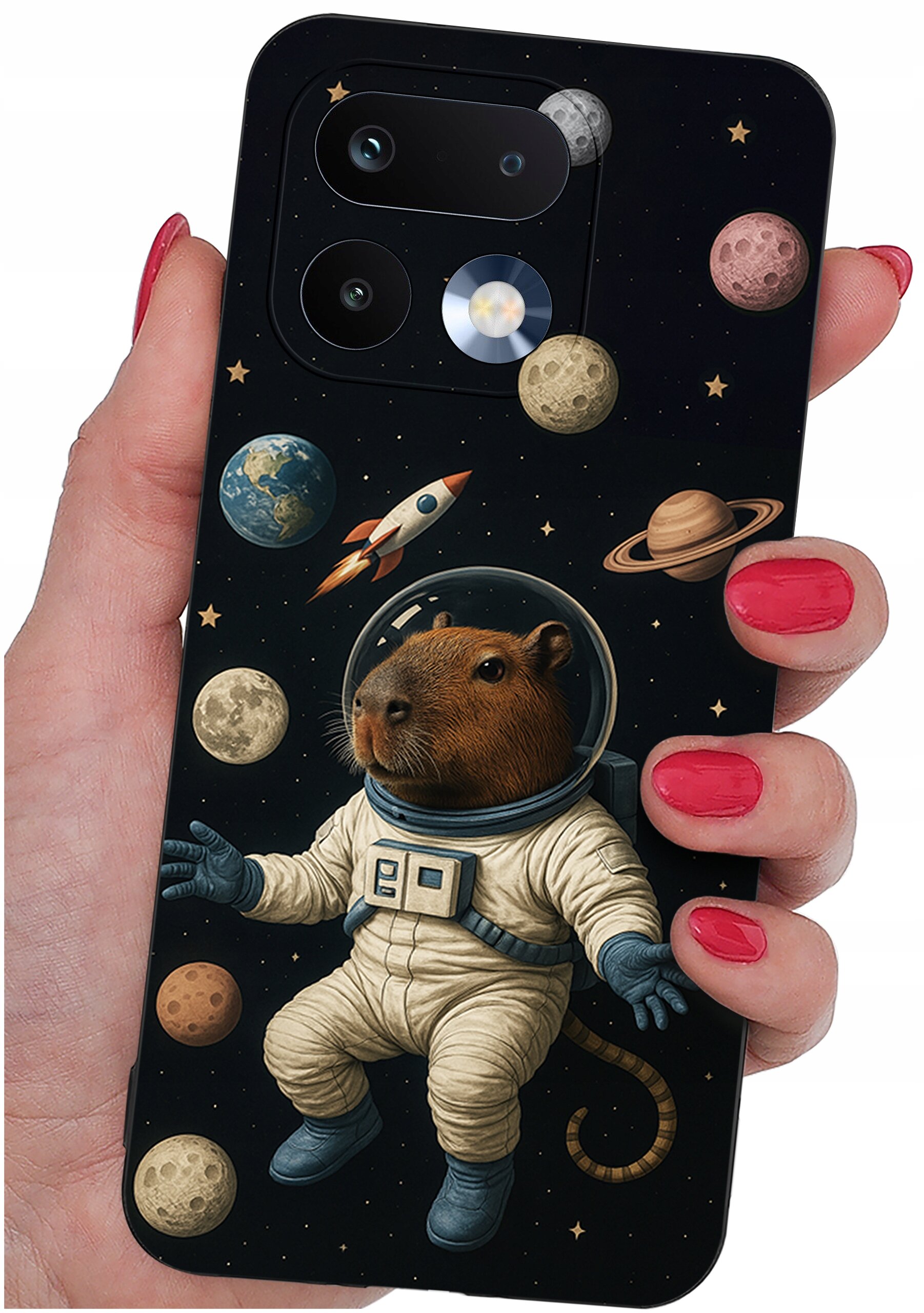 Etui na telefon z grafiką przedstawiającą kapibarę w skafandrze kosmicznym, otoczoną planetami i rakietą na tle gwiazd. Etui trzymane jest w dłoni z pomalowanymi na czerwono paznokciami.