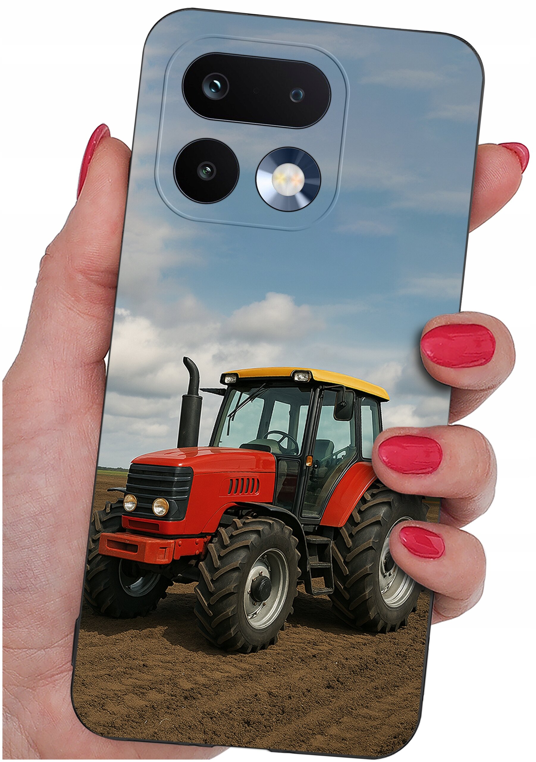 Etui na telefon z nadrukiem czerwonego traktora na tle pola i nieba, trzymane w dłoni z pomalowanymi na czerwono paznokciami.