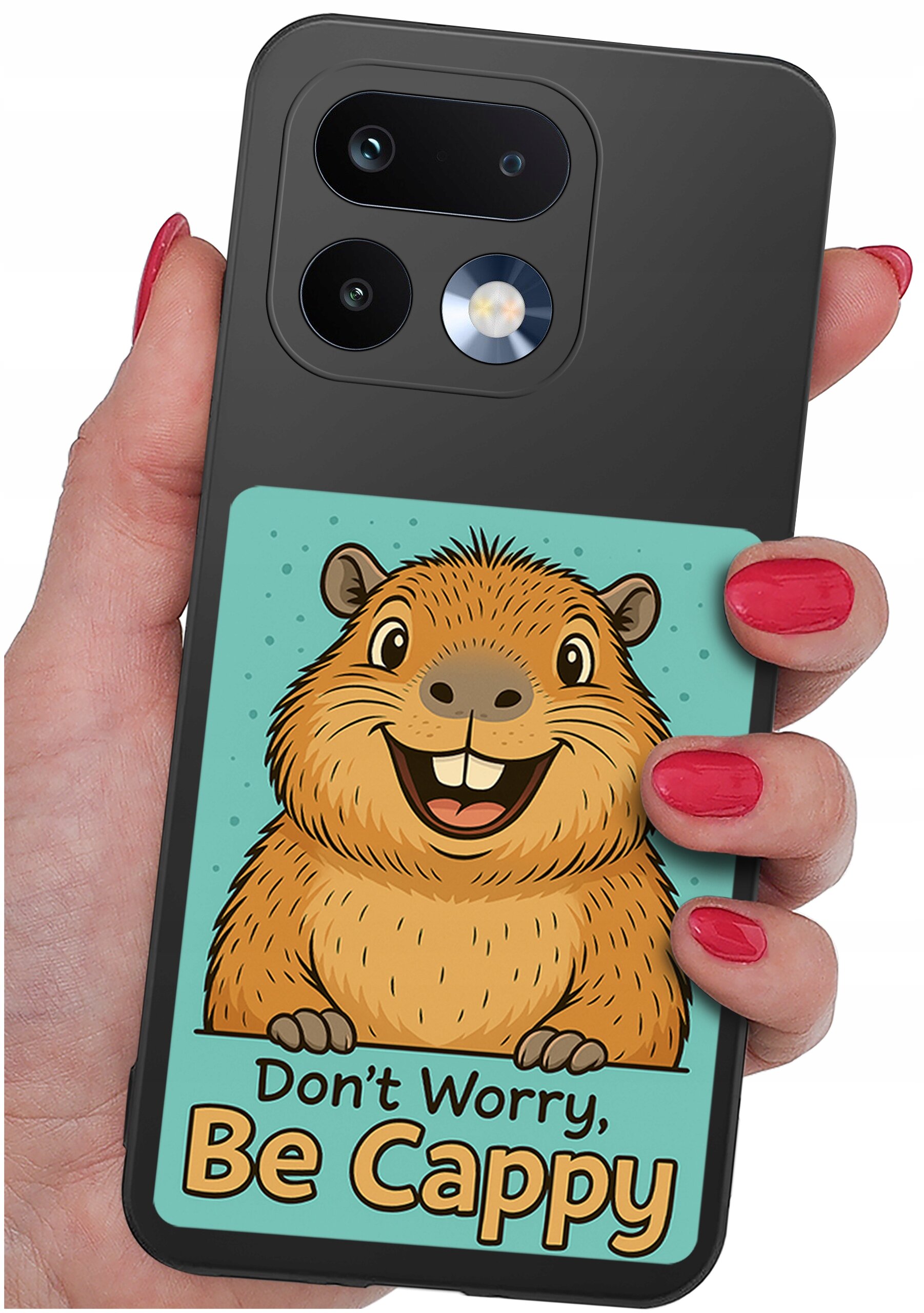 Osoba trzyma telefon z etui przedstawiającym rysunek uśmiechniętej kapibary na tle turkusowym z napisem \'Don\'t Worry, Be Cappy\'.