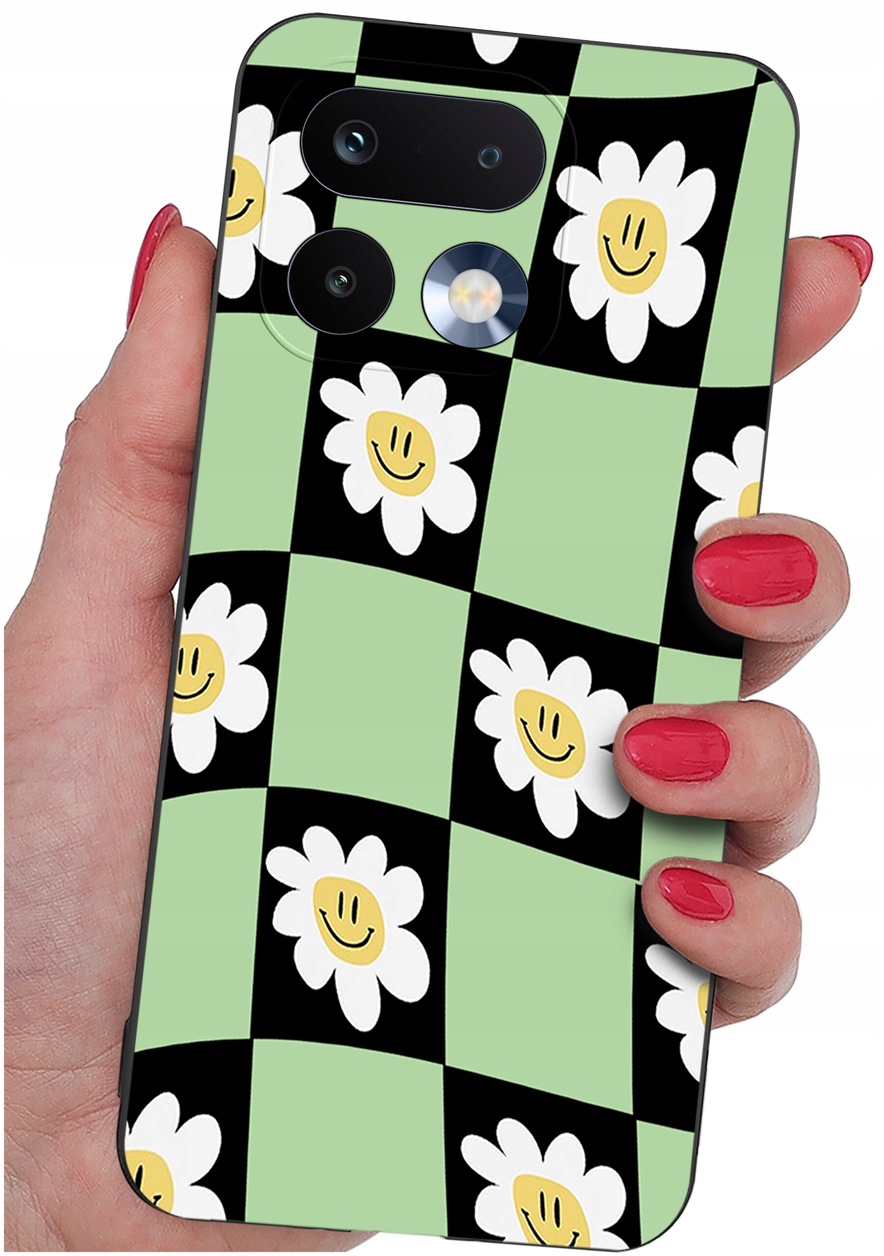 Etui na telefon z wzorem w kratkę, gdzie na zielonych i czarnych polach znajdują się białe kwiaty z uśmiechniętymi buźkami. Etui jest trzymane w dłoni z pomalowanymi na czerwono paznokciami.