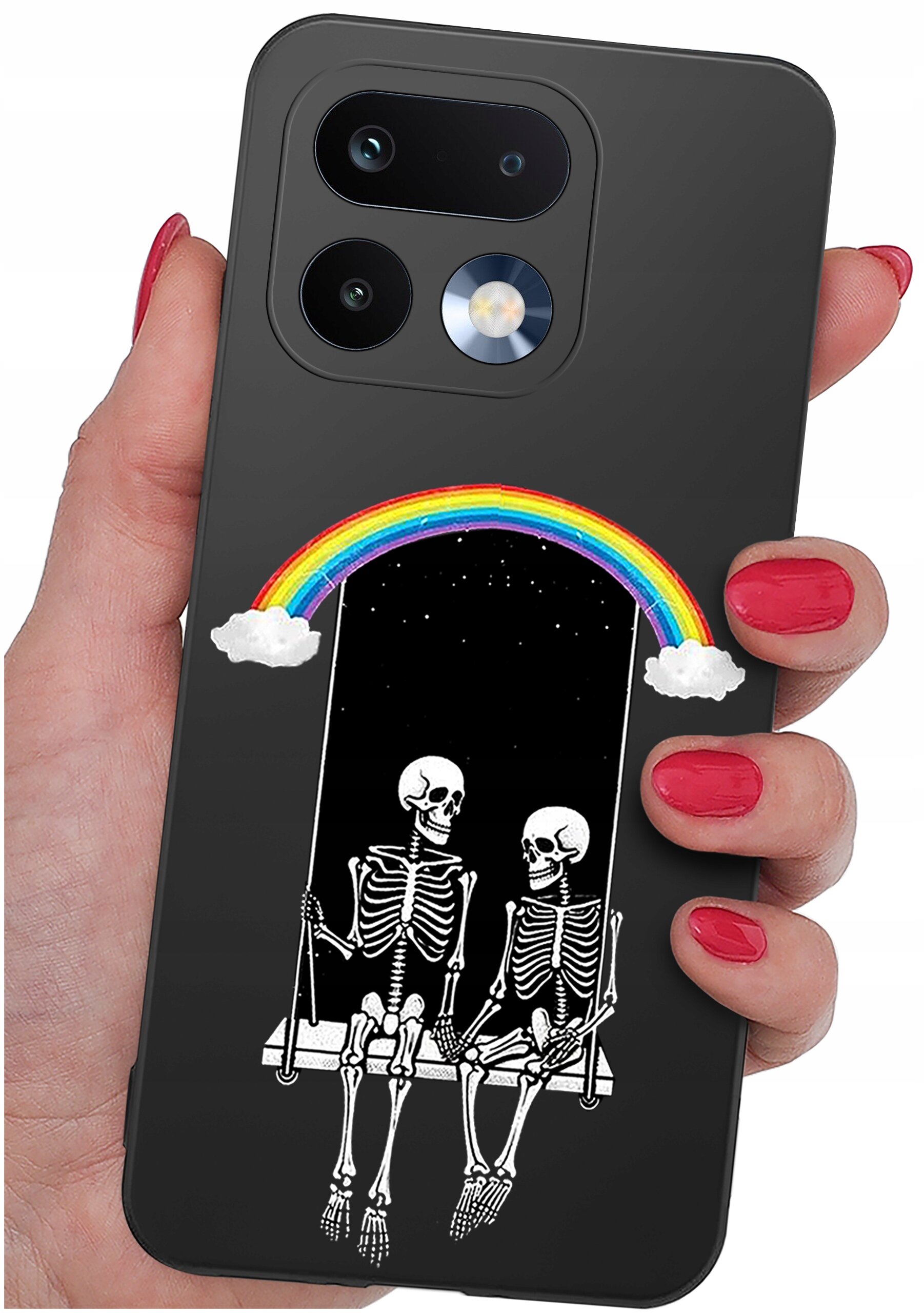 Etui na telefon z grafiką przedstawiającą dwa szkielety siedzące na huśtawce pod tęczą z chmurkami. Etui jest trzymane w dłoni z pomalowanymi na czerwono paznokciami.