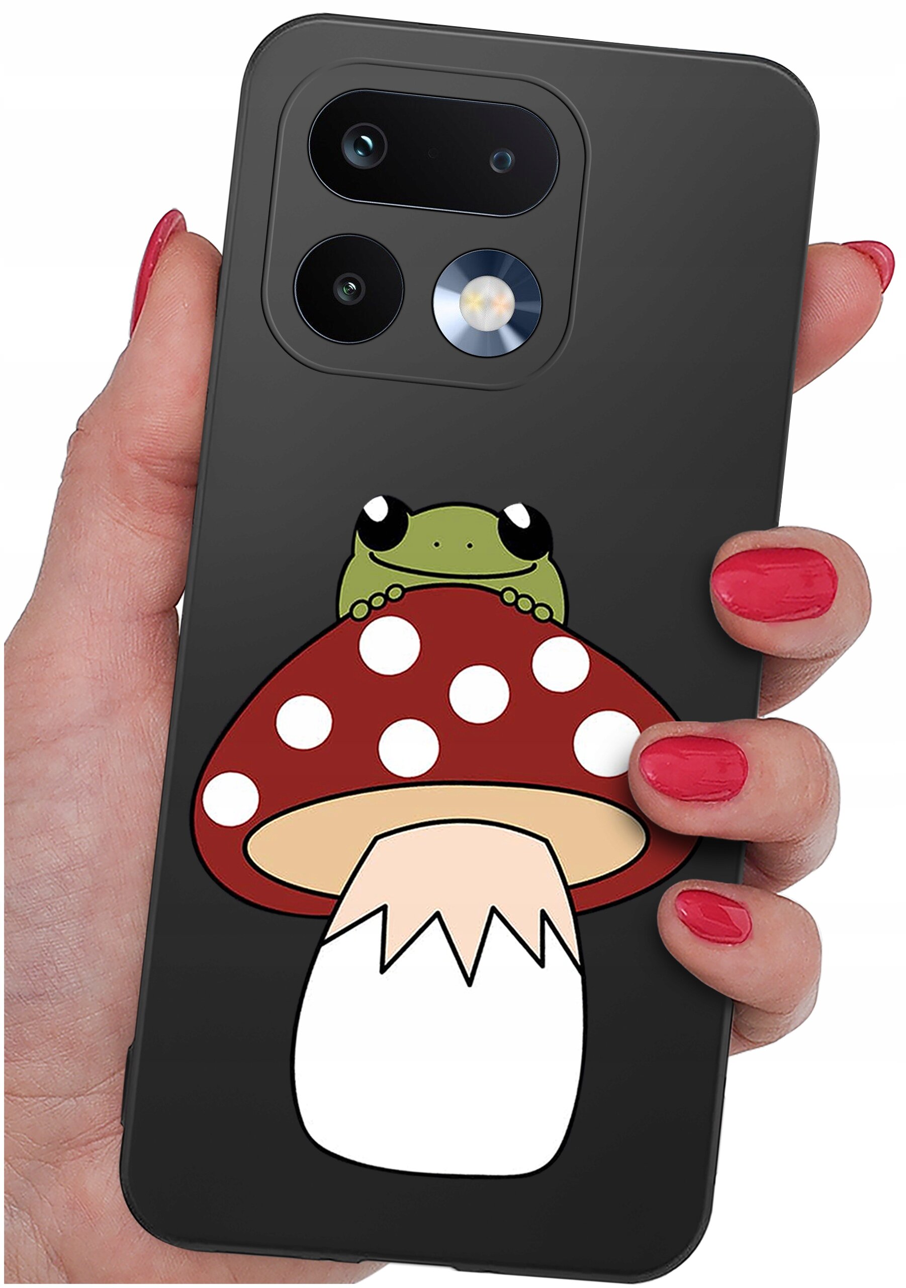 Osoba trzyma telefon z czarnym etui, na którym znajduje się grafika przedstawiająca żabę siedzącą na czerwonym muchomorze z białymi kropkami. Etui ma wycięcia na dwa obiektywy aparatu i lampę błyskową.