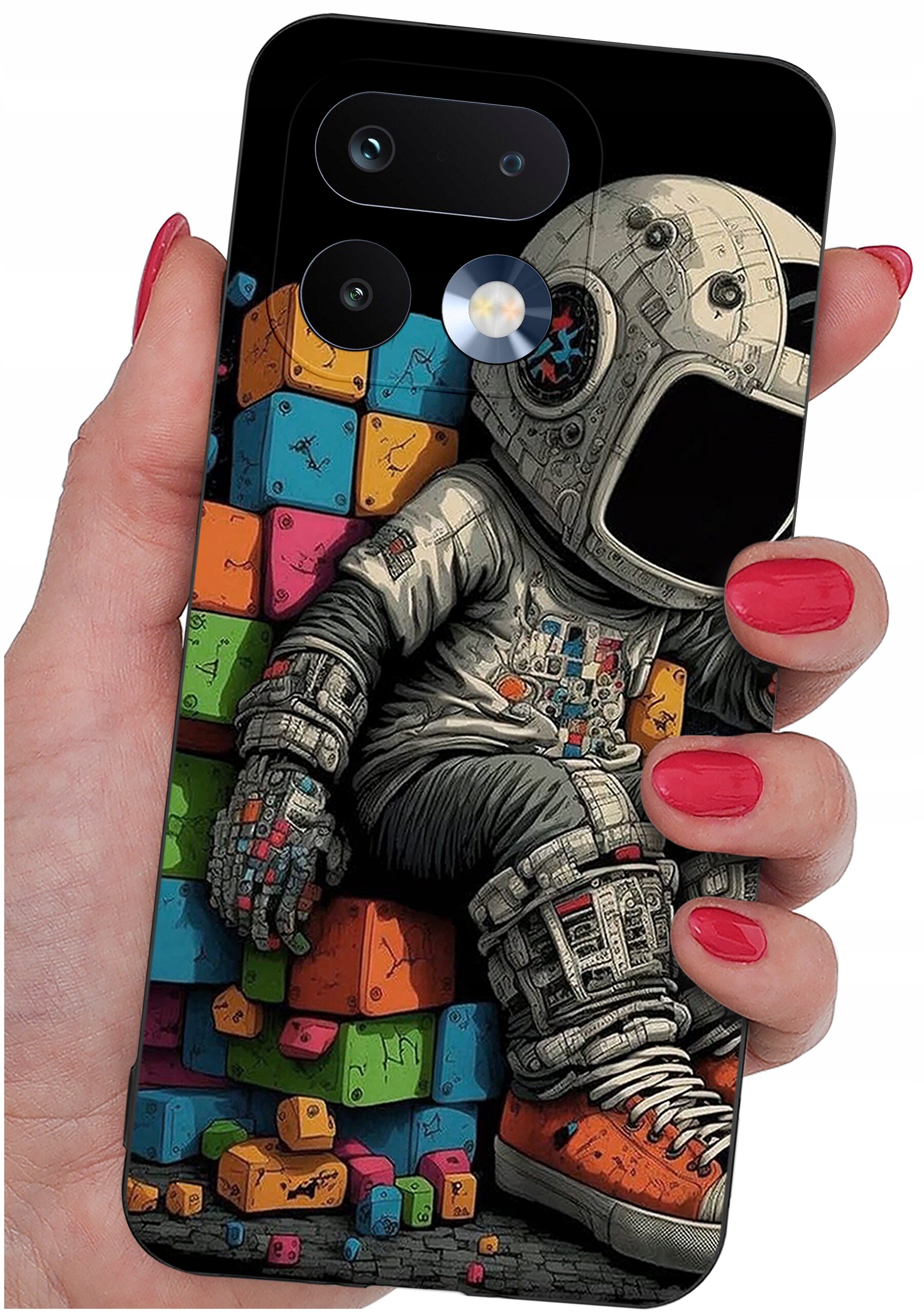 Etui na telefon z kolorowym nadrukiem przedstawiającym astronautę siedzącego na tle kolorowych klocków. Etui jest trzymane w dłoni z pomalowanymi na czerwono paznokciami.