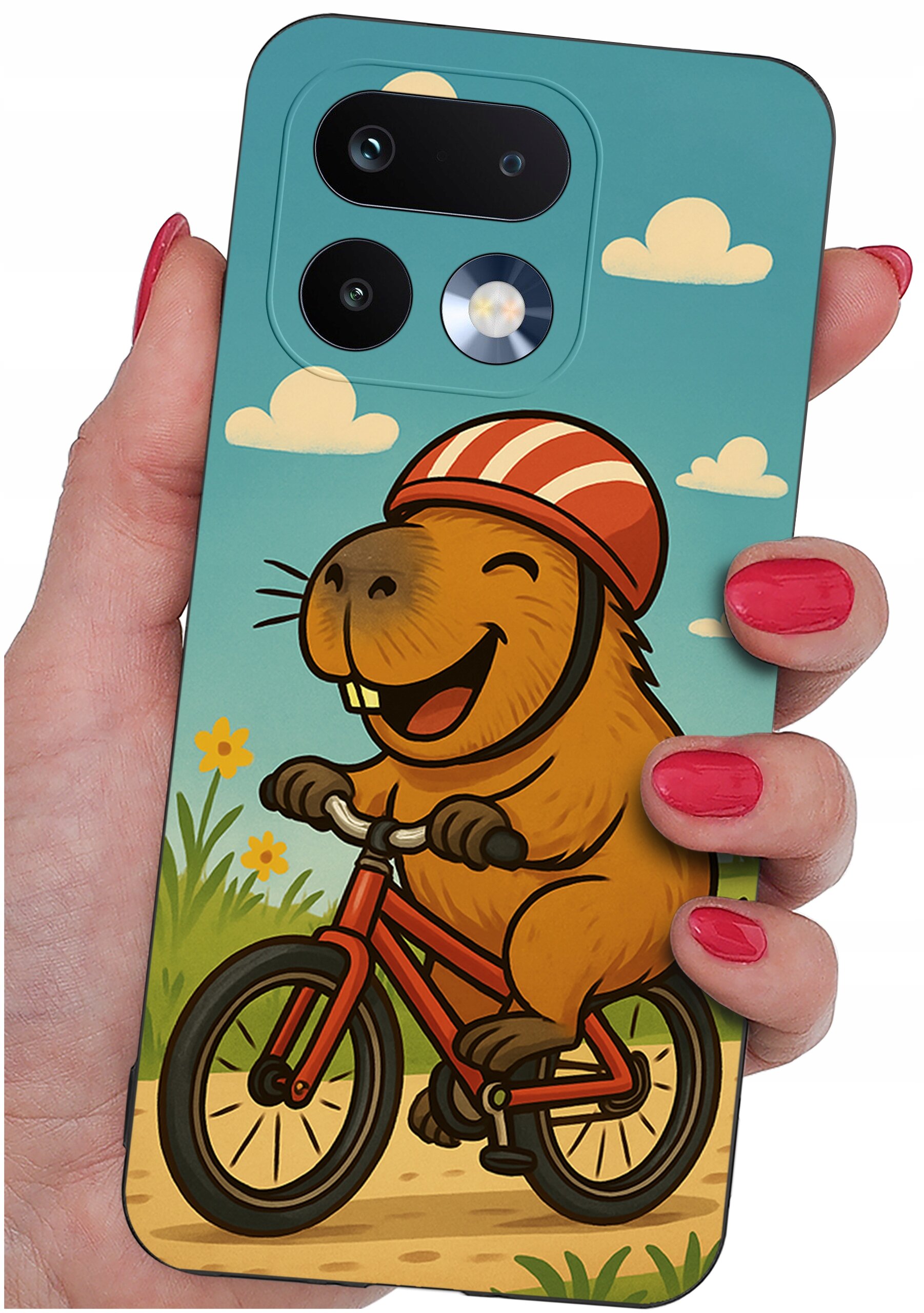 Etui na telefon z kolorowym nadrukiem przedstawiającym uśmiechniętego zwierzaka na rowerze w kasku, trzymane w dłoni z pomalowanymi na czerwono paznokciami. W tle widać niebieskie niebo z chmurkami i zieloną trawę z kwiatami.