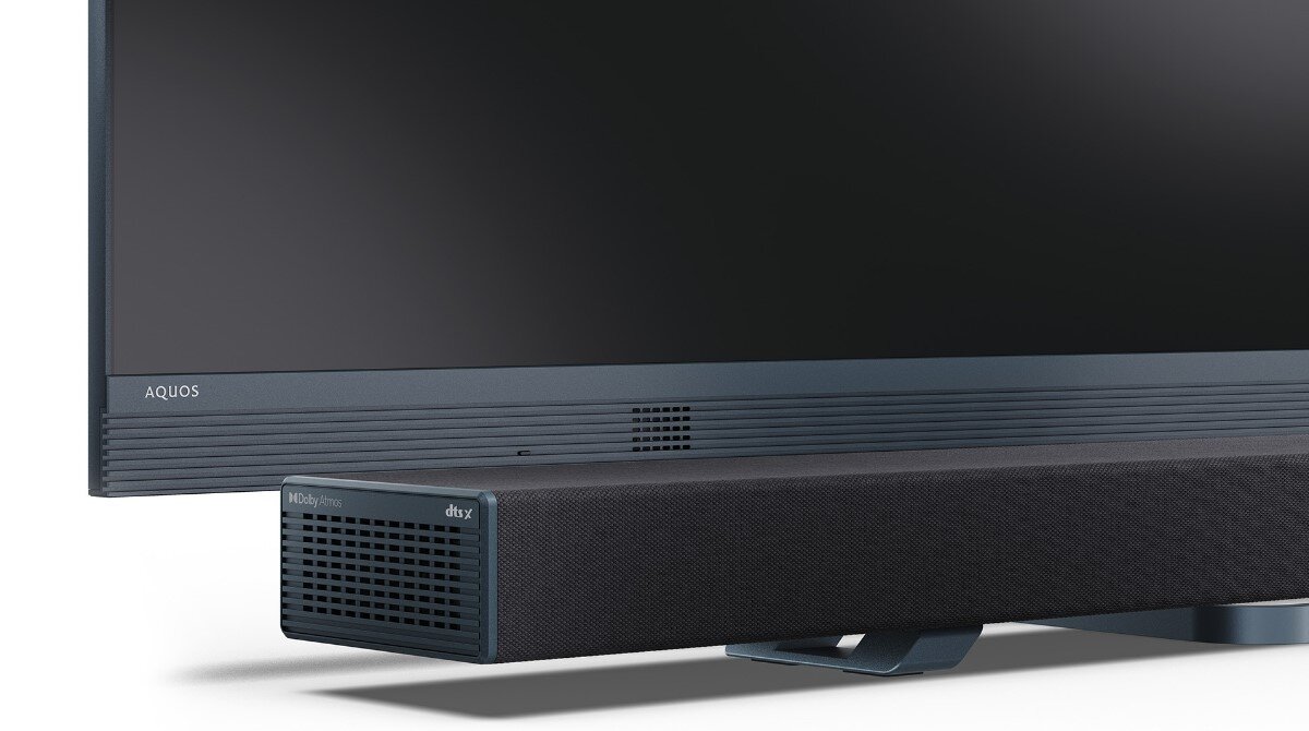 Na obrazie widoczny jest czarny soundbar z napisem \'media expert\' oraz \'dts x\', umieszczony przed telewizorem z logo \'AQUOS\'.