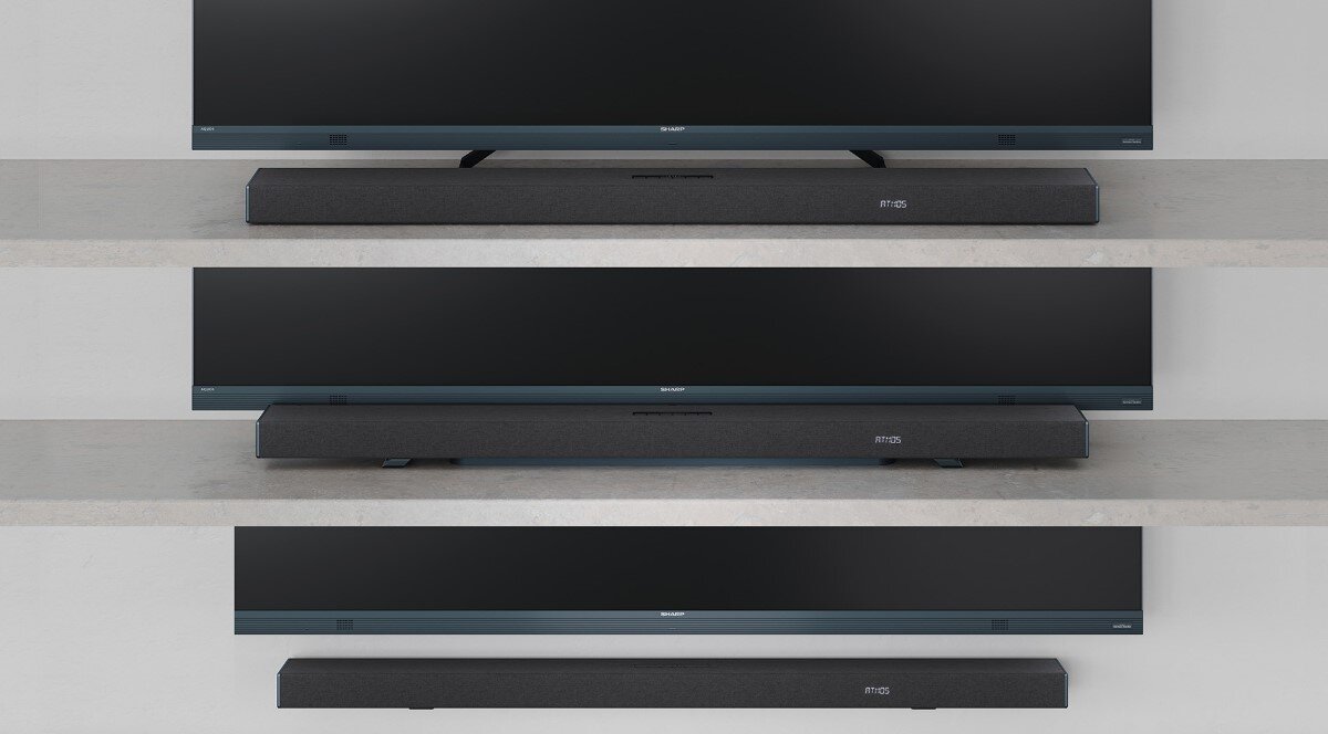 Na obrazie widoczny jest czarny soundbar umieszczony pod telewizorem na półce. Na soundbarze znajduje się logo \'SHARP\'.