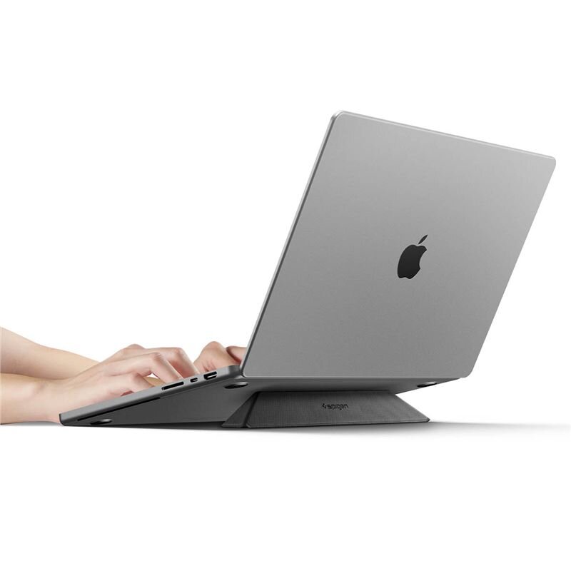 Laptop umieszczony na czarnym stojaku Spigen Slimfold, z widocznym logo jabłka na pokrywie. Osoba pisze na klawiaturze laptopa.