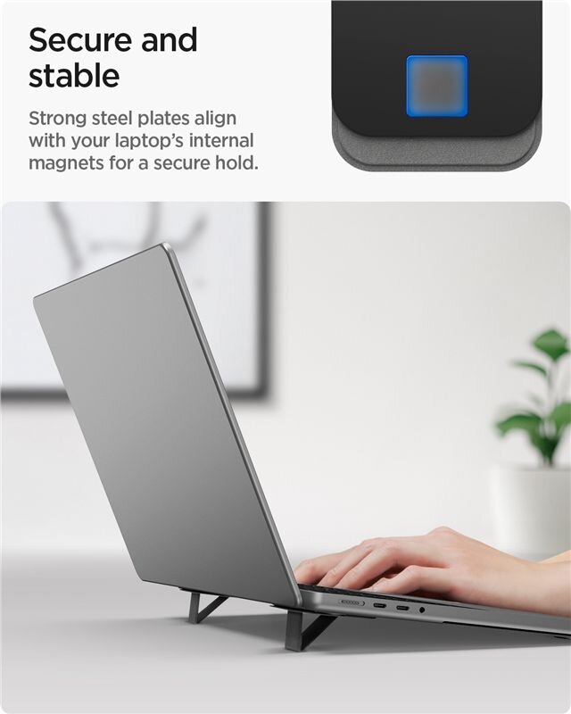 Na obrazie widać laptop ustawiony na czarnym stojaku, a w tle znajduje się roślina. Tekst na obrazie: \'Secure and stable. Strong steel plates align with your laptop\'s internal magnets for a secure hold.\'
