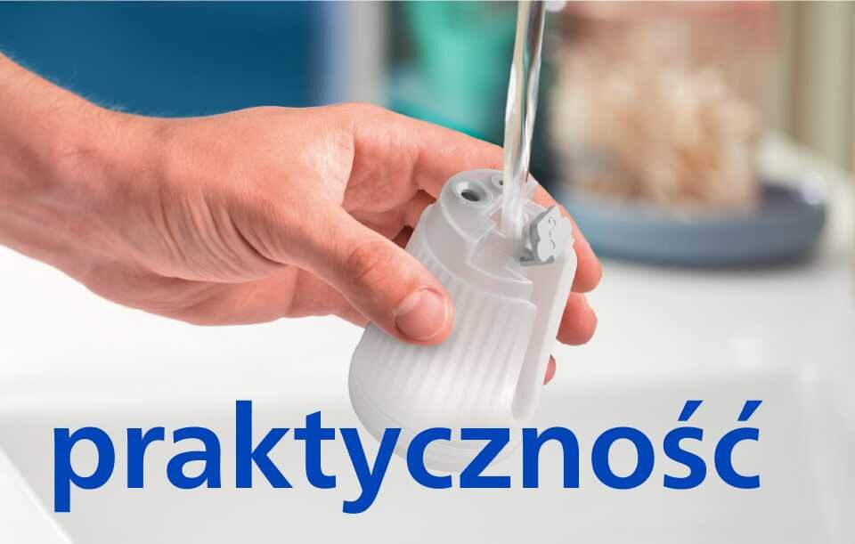 Osoba trzyma biały element urządzenia pod strumieniem wody. Na dole widoczny jest napis \'praktyczność\'.