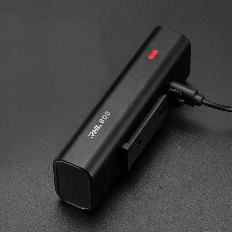 Czarna lampka rowerowa z napisem \'RHL 800\' i czerwonym wskaźnikiem, podłączona do kabla USB-C.
