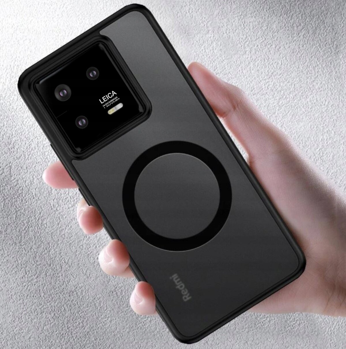 Osoba trzyma czarne etui na telefon z widocznym logo \'Redmi\' i okrągłym wzorem na tylnej części. W górnej części etui znajduje się aparat z trzema obiektywami i napisem \'LEICA\'.
