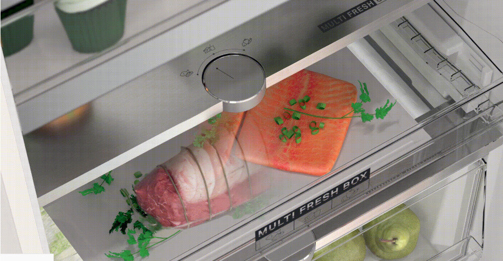 Wnętrze lodówki z widoczną szufladą oznaczoną jako \'MULTI FRESH BOX\', w której znajdują się kawałki mięsa i łososia udekorowane ziołami. W dolnej części widoczne są dwie zielone gruszki.