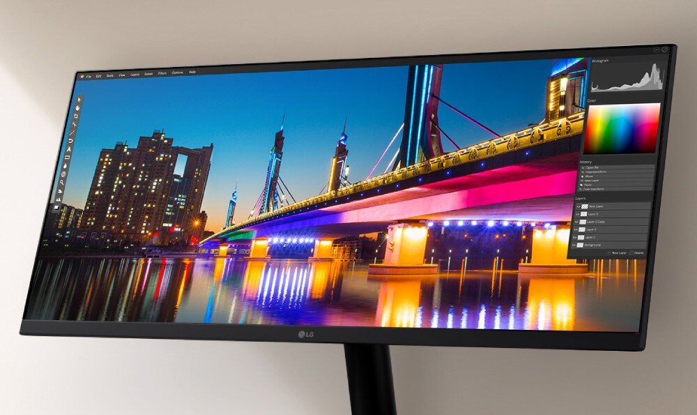 Monitor wyświetla kolorowy obraz miasta z mostem oświetlonym różnobarwnymi światłami. Na ekranie widoczne są również narzędzia do edycji zdjęć oraz histogram.