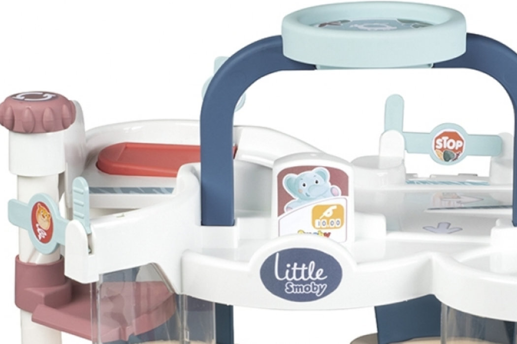 Zabawka przedstawia wielopoziomowy garaż z elementami w kolorach białym, niebieskim i czerwonym, z widocznym logo \'Little Smoby\'. Na jednym z poziomów znajduje się znak \'STOP\' oraz obrazek z niebieskim misiem.