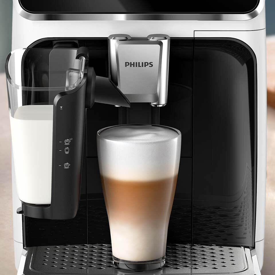 Ekspres do kawy z logo PHILIPS przygotowuje kawę z mleczną pianką w szklance. Obok znajduje się pojemnik na mleko z oznaczeniami poziomu napełnienia.