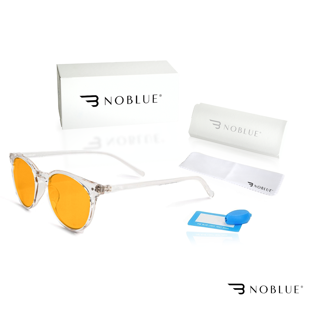 Na obrazie widoczne są okulary z pomarańczowymi soczewkami, pudełko, etui i ściereczka z logo \'NOBLUE\'. Obok znajduje się niebieski element testowy z napisem \'THE BLUE LIGHT TEST AREA\'.