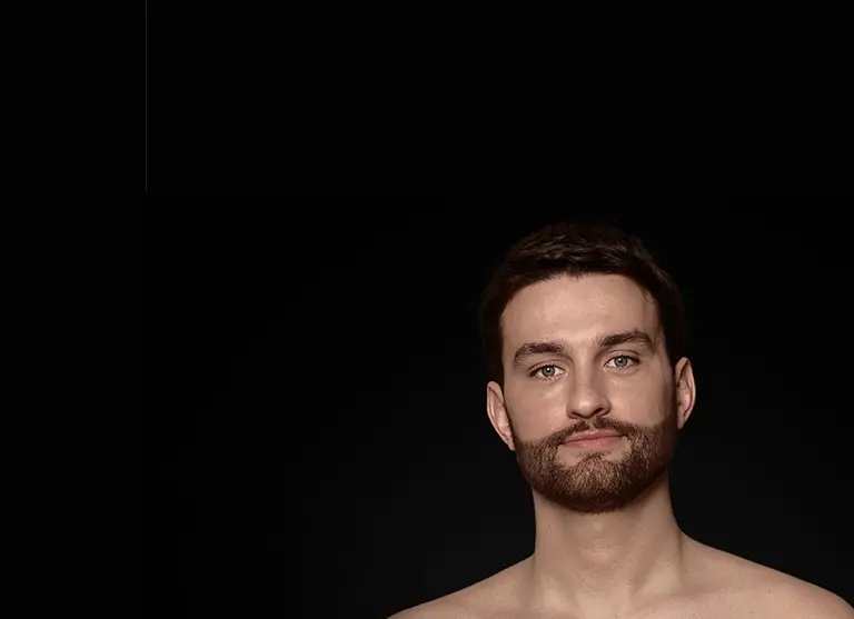 Mężczyzna z krótką brodą na ciemnym tle, patrzący prosto przed siebie.