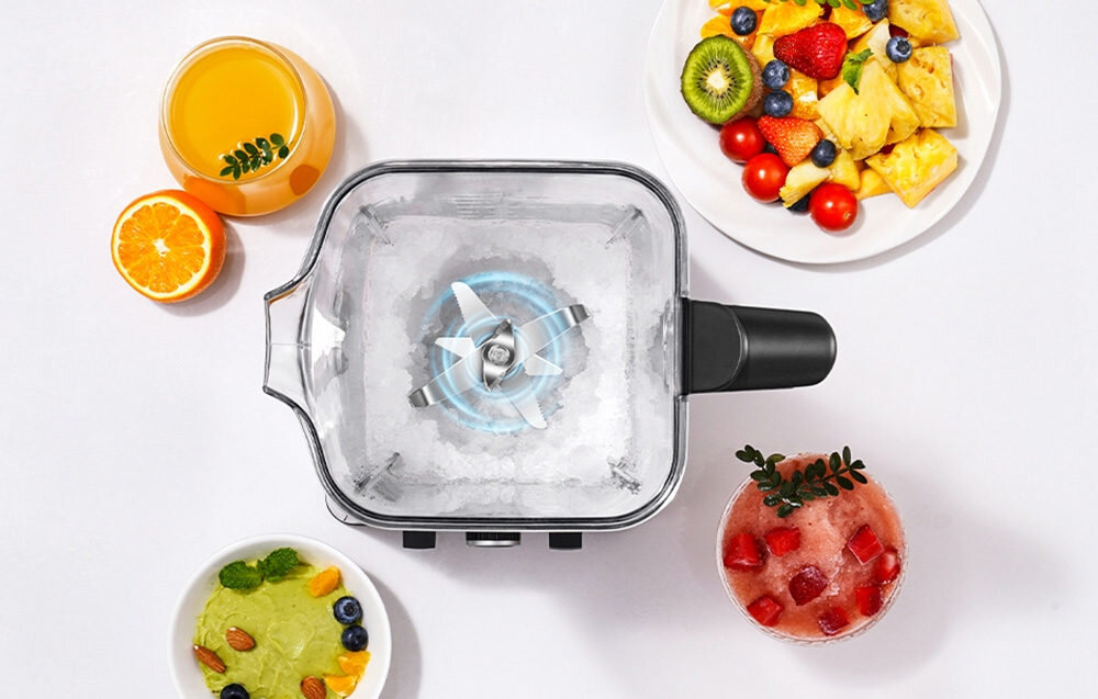 Na obrazie widoczny jest blender kielichowy z ostrzami w środku, otoczony różnymi potrawami i napojami, w tym sokiem pomarańczowym, sałatką owocową i koktajlem. Blender jest umieszczony na białym tle.