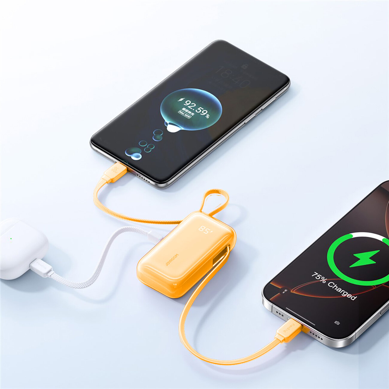 Na obrazie widać powerbank w kolorze pomarańczowym z wbudowanymi kablami USB-C i Lightning, podłączony do dwóch smartfonów. Na ekranach telefonów widoczne są wskaźniki ładowania: 92.59% i 75% Charged.
