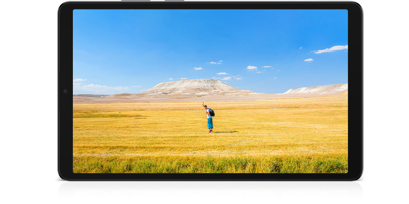 Tablet z wyświetlaczem pokazującym krajobraz z osobą stojącą na polu, w tle widoczne wzgórza i niebo z chmurami. Obudowa tabletu jest srebrna.