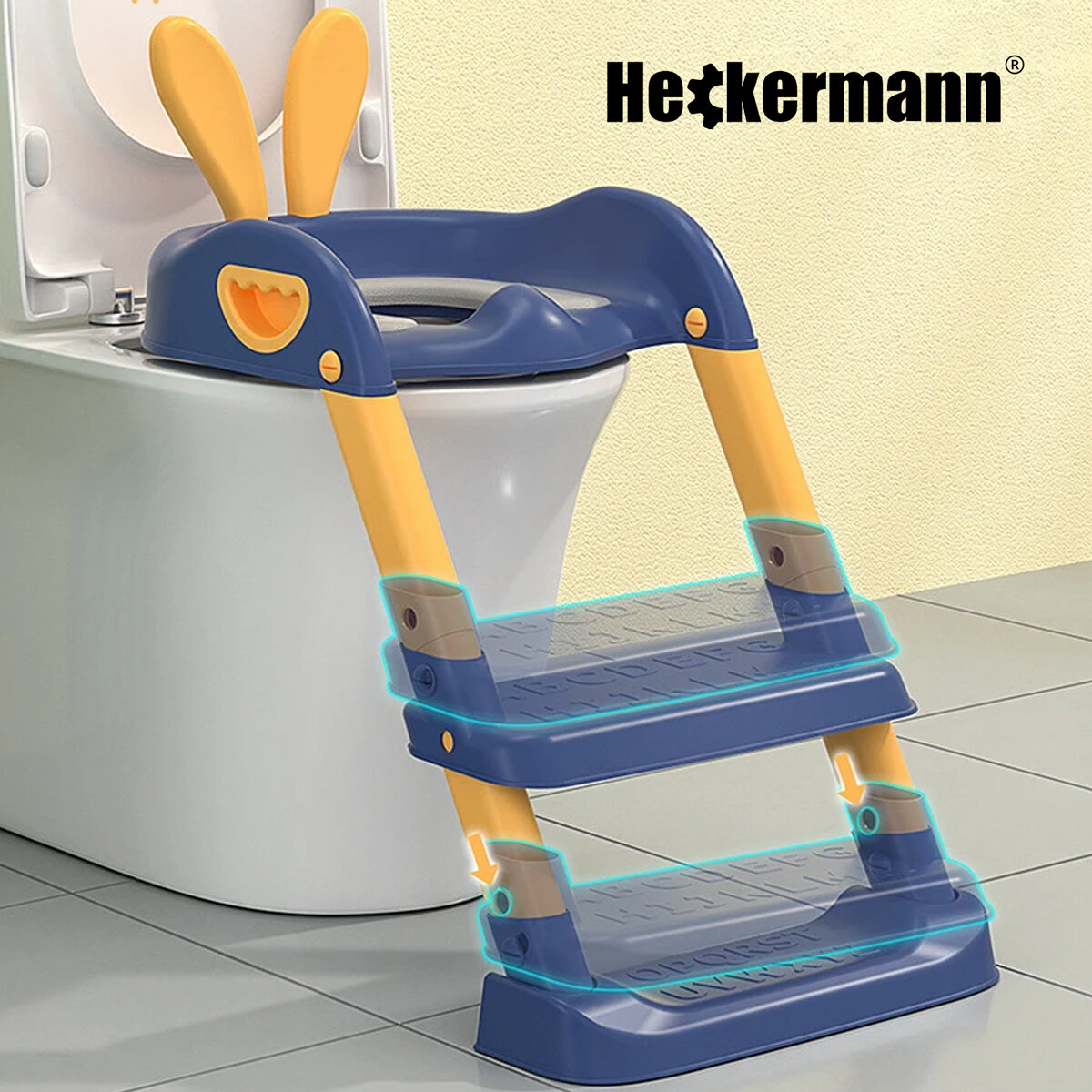 Na obrazie widoczna jest niebieska nakładka na sedes z żółtymi uchwytami i stopniami, umieszczona na toalecie. W tle znajduje się logo \'Heckermann\'.