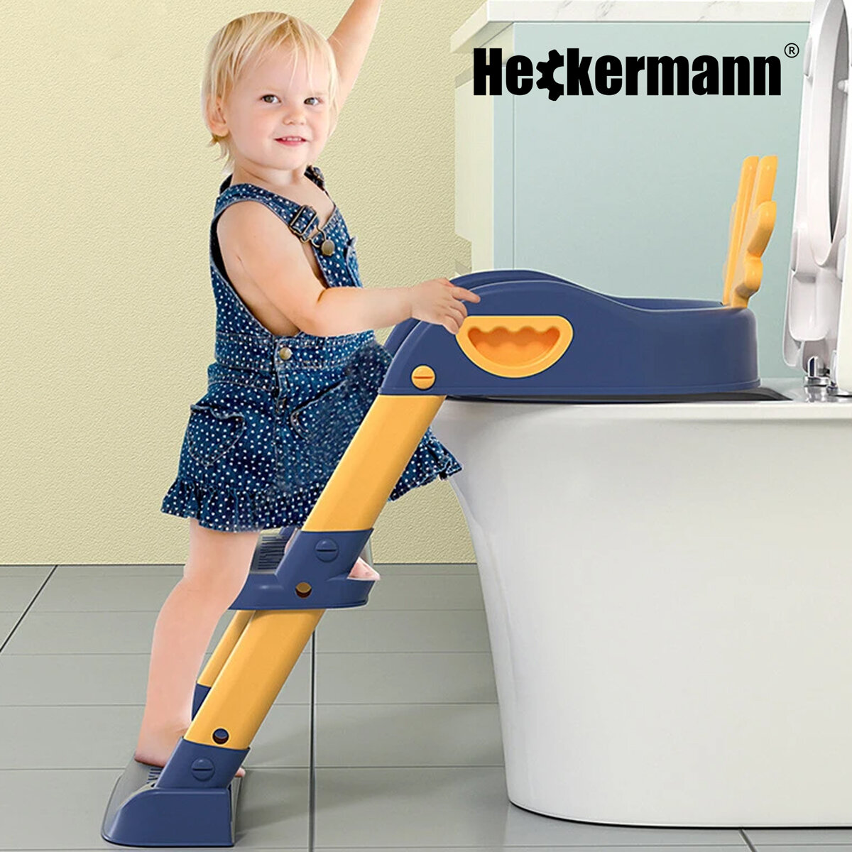 Dziecko stoi przy toalecie z niebieską nakładką Heckermann, która ma żółte elementy i schodki. Logo Heckermann widoczne jest w górnym rogu obrazu.