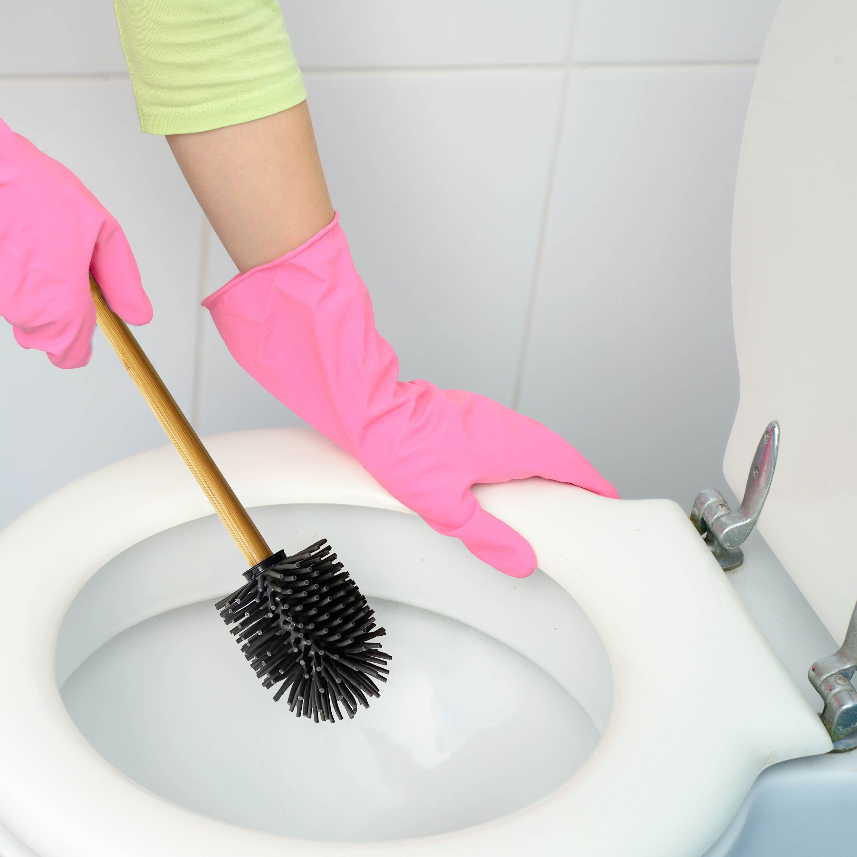 Osoba w różowych rękawiczkach trzyma szczotkę do WC z czarną silikonową główką i drewnianym uchwytem, czyszcząc toaletę.