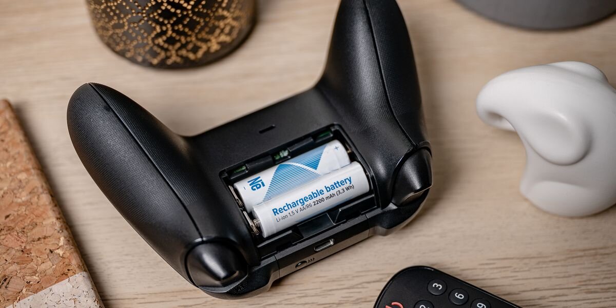 Czarny kontroler z otwartą komorą na baterie, w której znajdują się dwa akumulatory z widocznym napisem \'Rechargeable battery 1.2V AA 2200 mAh (2.6 Wh)\'.