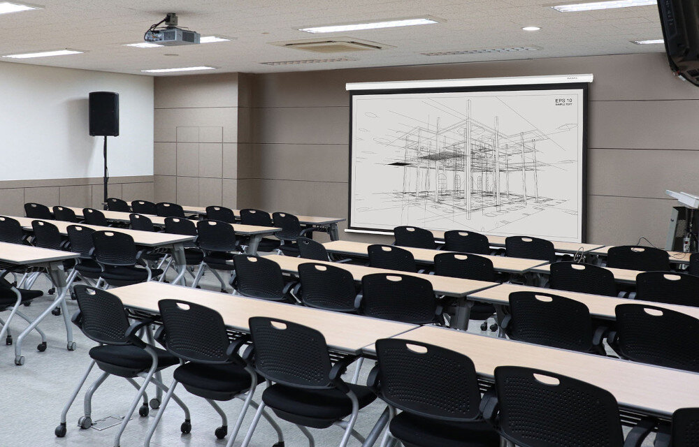 Sala konferencyjna z rzutnikiem i ekranem projekcyjnym, na którym wyświetlany jest schematyczny rysunek konstrukcji. W pomieszczeniu znajdują się rzędy stołów i krzeseł, a na ścianie widoczne jest logo \'media expert\'.