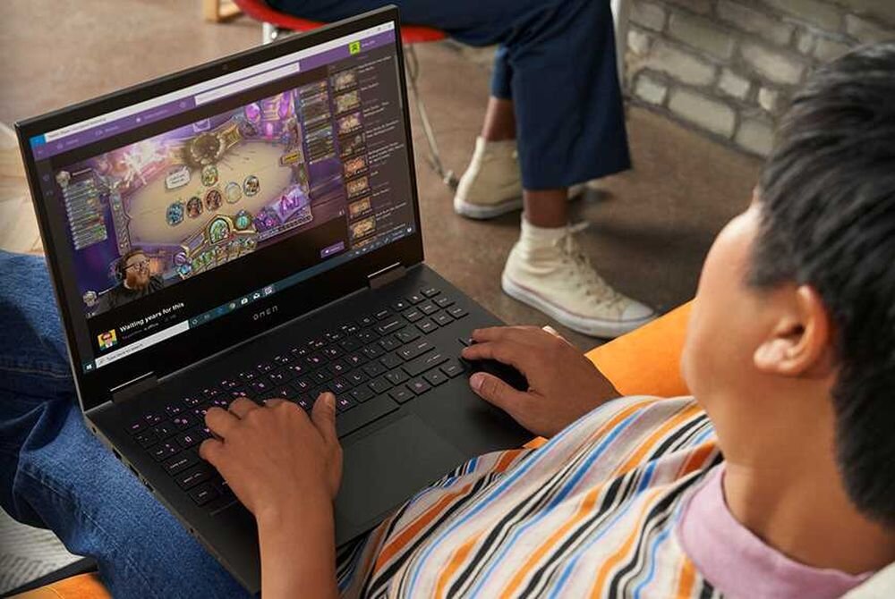 Osoba korzysta z laptopa, na którym wyświetlana jest gra komputerowa. Na obudowie laptopa widoczne jest logo \'OMEN\'.