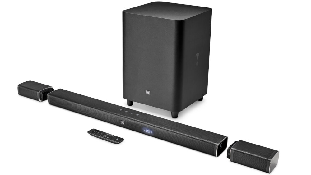 Na obrazie znajduje się czarny soundbar z subwooferem i dwoma głośnikami satelitarnymi. Na wyświetlaczu soundbara widoczny jest napis \'HDMI 2\'.