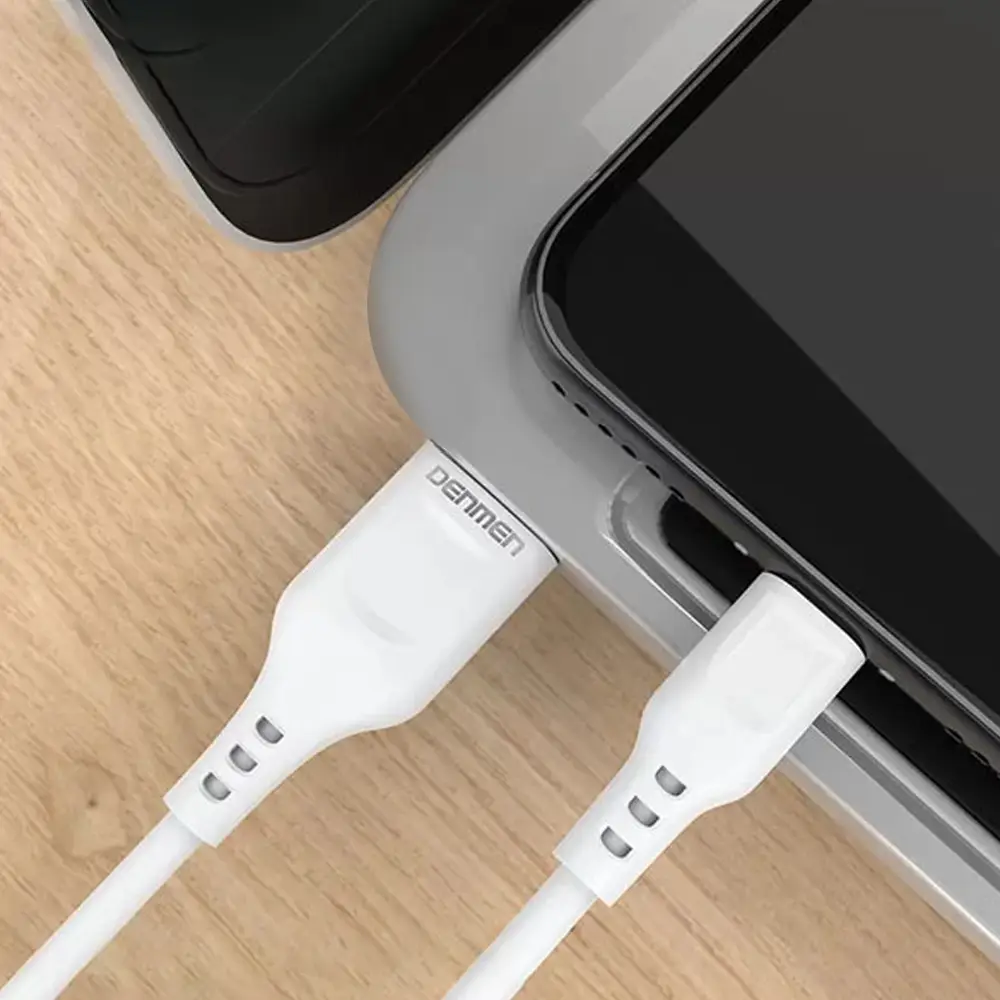 Na drewnianym blacie leży urządzenie elektroniczne z podłączonym białym kablem USB, na którym widnieje napis \'DENMEN\'.