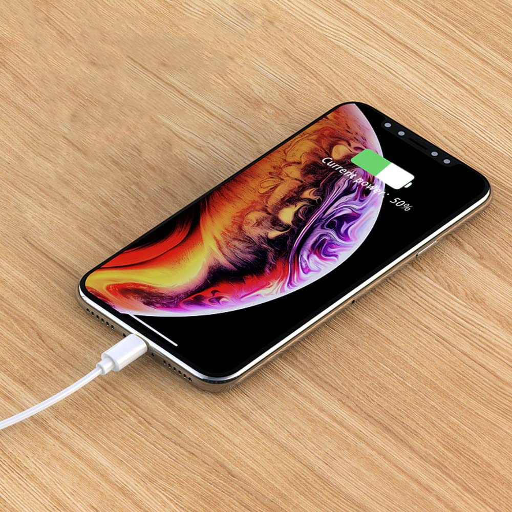 Na drewnianej powierzchni leży smartfon z kolorowym wyświetlaczem, do którego podłączony jest biały kabel. Na ekranie widoczny jest wskaźnik ładowania z napisem \'Current Power: 50%\'.