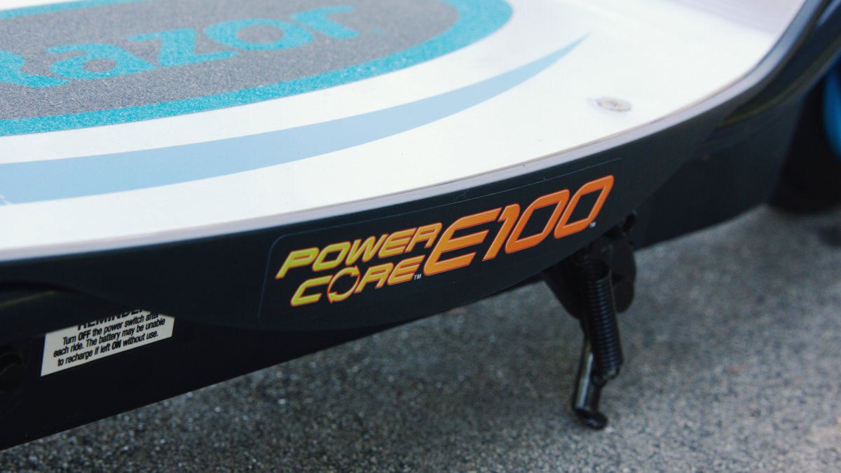 Zbliżenie na część hulajnogi elektrycznej z widocznym napisem \'POWER CORE E100\'. Na powierzchni podestu widoczny jest fragment logo \'razor\'.