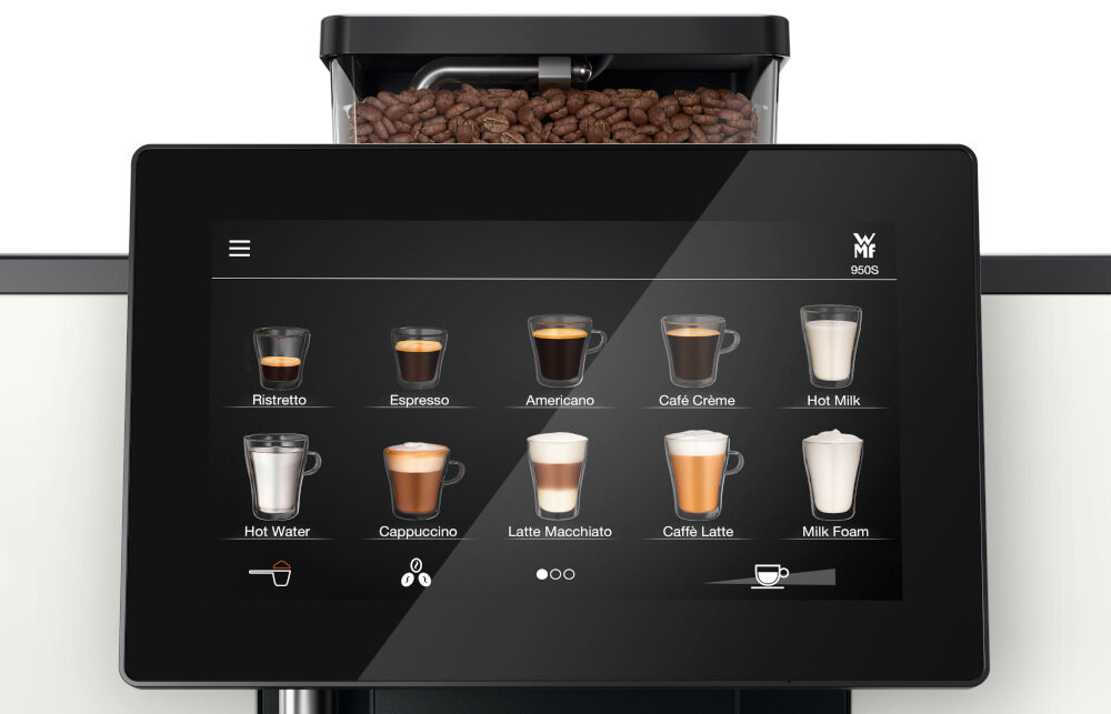 Na ekranie ekspresu do kawy widoczne są ikony różnych napojów, takich jak Ristretto, Espresso, Americano, Café Crème, Hot Milk, Hot Water, Cappuccino, Latte Macchiato, Caffè Latte i Milk Foam. Logo \'WMF\' znajduje się w prawym górnym rogu ekranu, a nad nim widoczne są ziarna kawy w pojemniku.