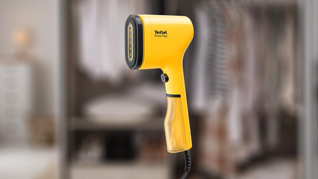 Żółta parownica do ubrań z napisem \'Tefal Pure Pop\' na obudowie. W tle widoczna jest rozmyta szafa z ubraniami.