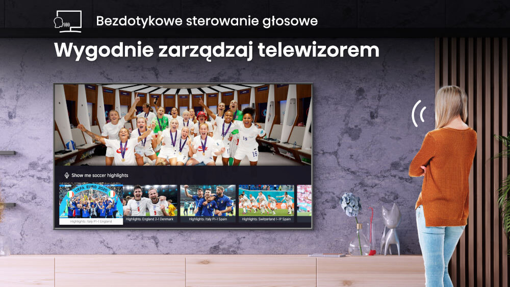 Na ścianie wisi telewizor wyświetlający obraz z drużyną sportową w szatni oraz miniaturki z meczami piłki nożnej. Nad telewizorem widnieje tekst: \'Bezdotykowe sterowanie głosowe Wygodnie zarządzaj telewizorem\'.