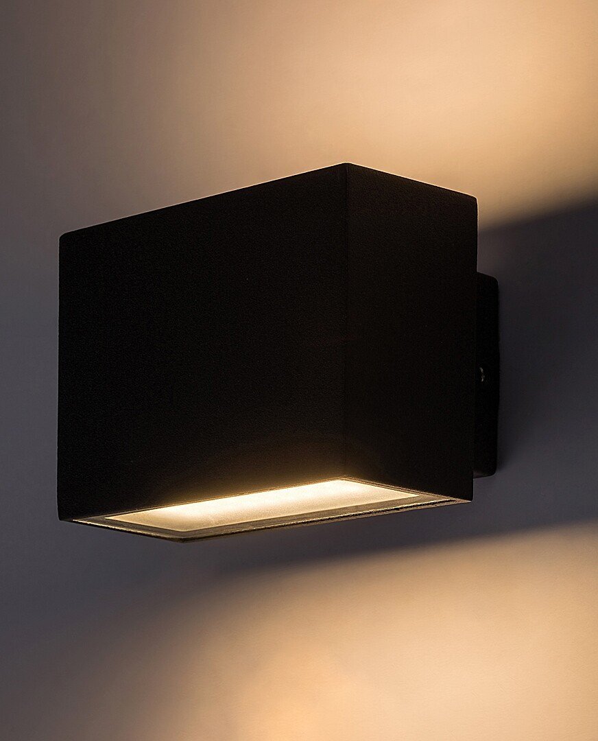 Czarna, prostokątna lampa ścienna emituje światło w górę i w dół, tworząc efektowne oświetlenie na ścianie.