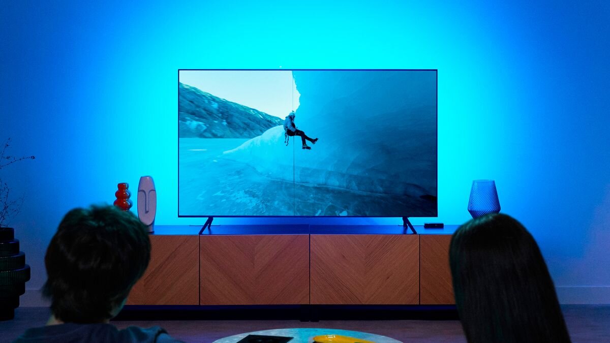 Taśma LED PHILIPS SMART HDMI 2.0 Sync Box Kit 40 - 50 929004772121 1.9 m Bluetooth/Wi-Fi, synchronizacja, obraz, kino, gry, Para ogląda telewizję z niebieskim podświetleniem ścian.