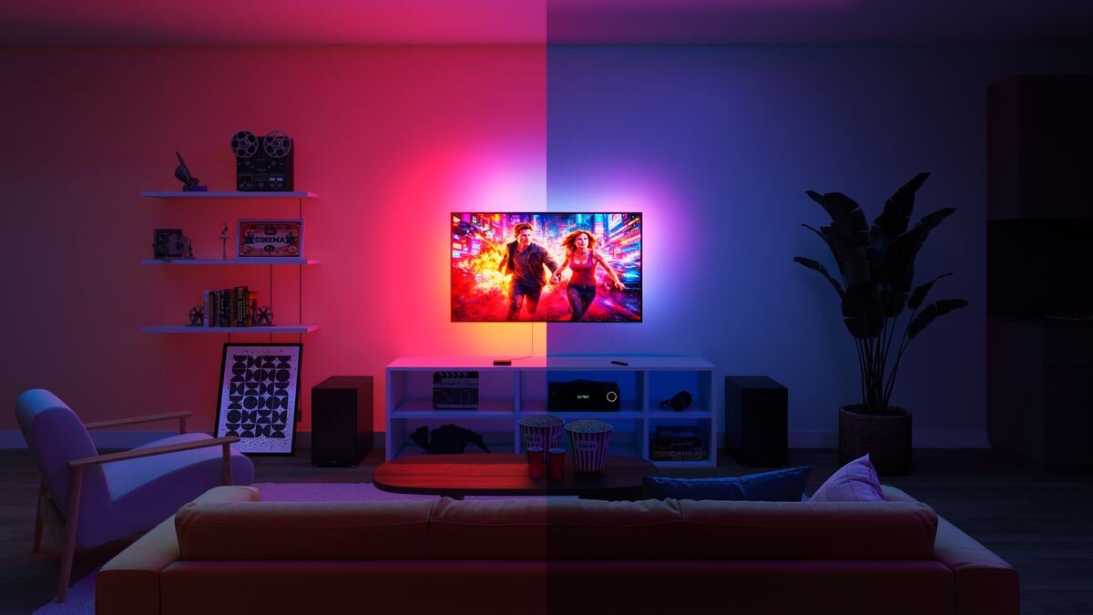 Pokój dzienny z telewizorem na środku, emitującym kolorowe światło na ścianę. Po lewej stronie światło jest różowe, a po prawej niebieskie; na półkach znajdują się książki i dekoracje.
