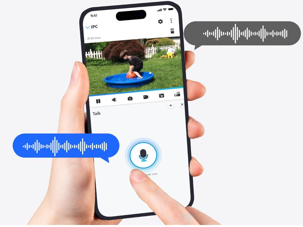 Osoba trzyma smartfon z aplikacją pokazującą obraz z kamery, na którym dziecko bawi się w niebieskim basenie. Na ekranie widoczne są ikony sterowania oraz przycisk mikrofonu z napisem \'Talk\'.