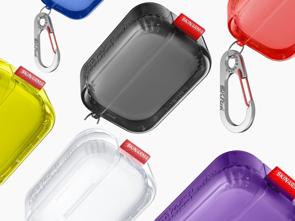 Na obrazie widoczne są różnokolorowe etui na słuchawki z logo \'SKINARMA\' na czerwonych etykietach. Każde etui ma przezroczystą powierzchnię i metalowy karabińczyk.