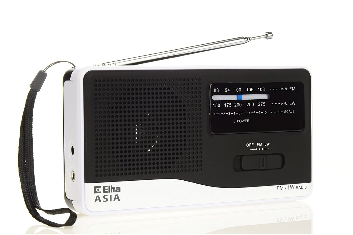 Białe radio analogowe z czarnym panelem przednim, posiada antenę teleskopową i pasek do przenoszenia. Na panelu widoczne są napisy: \'Eltra ASIA\', \'FM/LW RADIO\', oraz skala częstotliwości FM i LW.