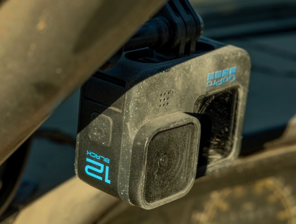 Kamera sportowa z widocznym napisem \'12 BLACK\' oraz logo \'gopro\'. Urządzenie jest zamontowane na uchwycie i pokryte lekkim kurzem.