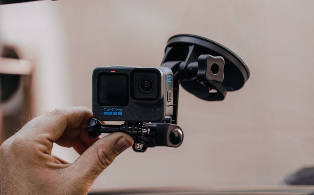 Osoba trzyma kamerę sportową zamontowaną na przyssawce. Na kamerze widoczne jest logo GoPro i oznaczenie modelu \'12\'.