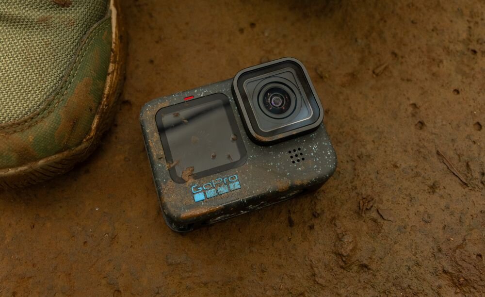 Kamera sportowa leży na ziemi, obok widoczny jest fragment buta. Na kamerze widoczne jest logo \'GoPro\'.