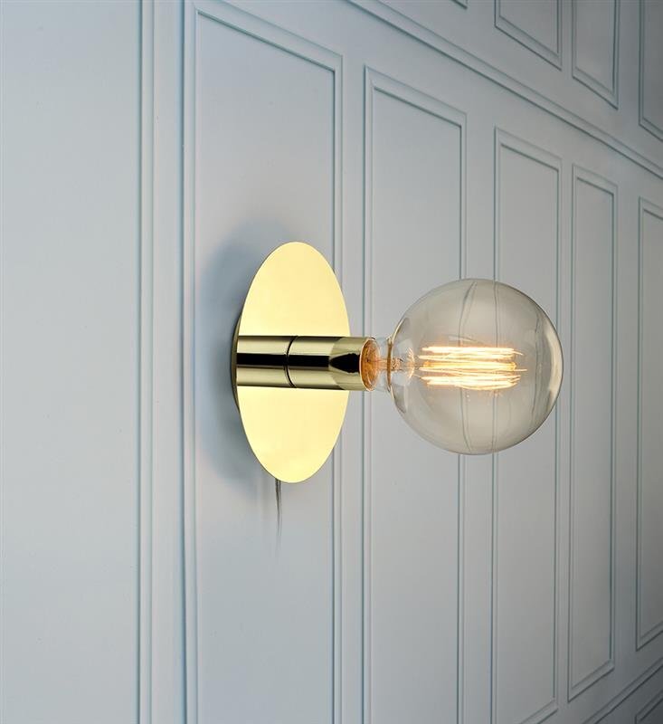 Na obrazie widoczna jest nowoczesna lampa ścienna z okrągłą, złotą podstawą i dużą, przezroczystą żarówką. Lampa zamontowana jest na ścianie z panelami o prostokątnych wzorach.